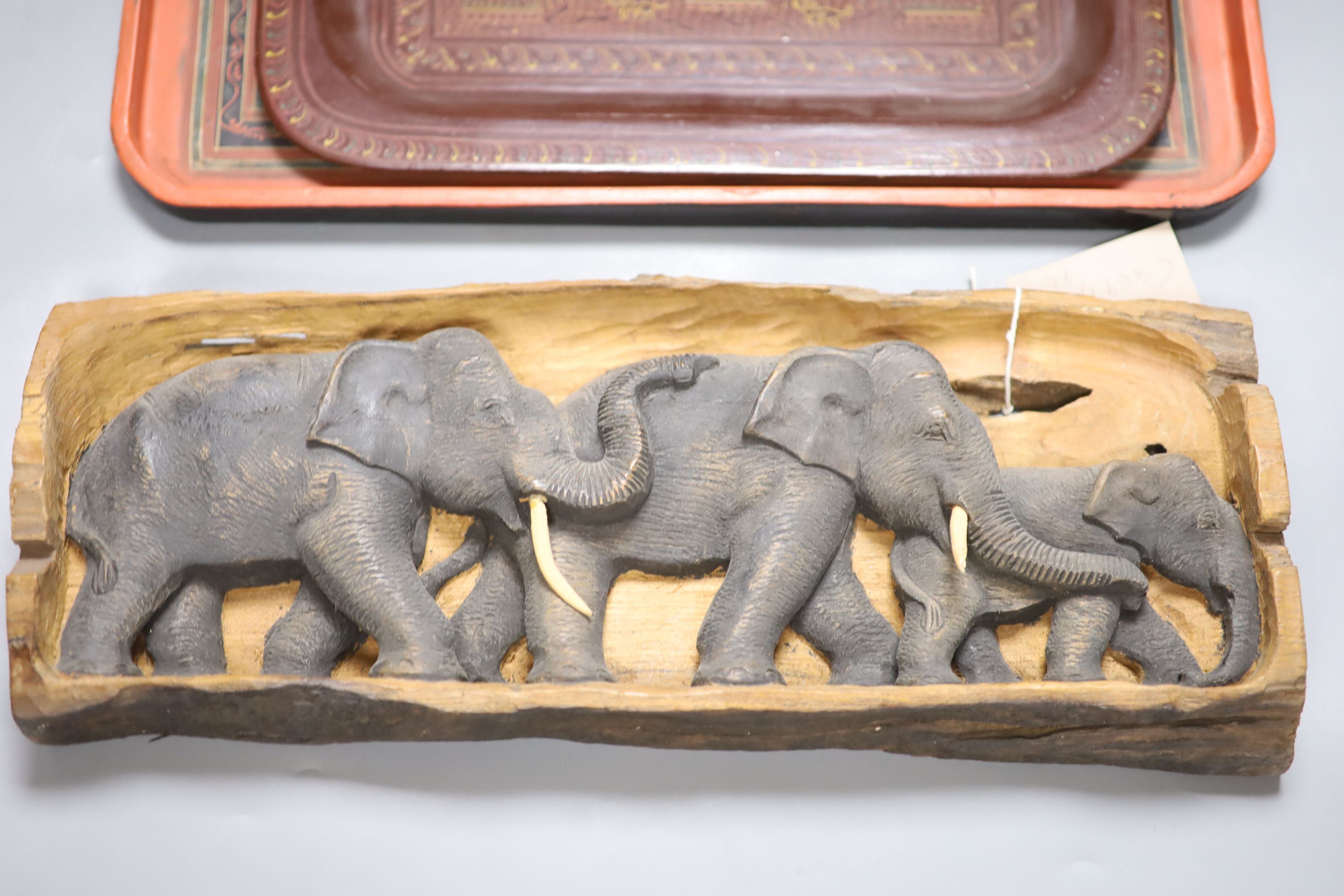 An African hardwood carving of a herd of elephants, and two papier mache trays, largest 46cm